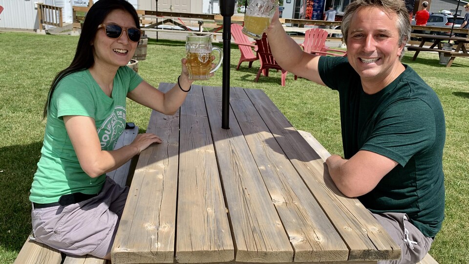 Deux personnes lèvent leur bière sur une terrasse. 