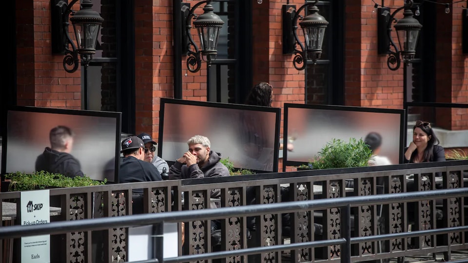 Des clients sont assis à des tables séparées par des panneaux translucides sur une terrasse de restaurant.