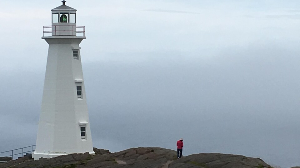 Un phare avec une personne marchant sur des rochers sous un ciel de plomb