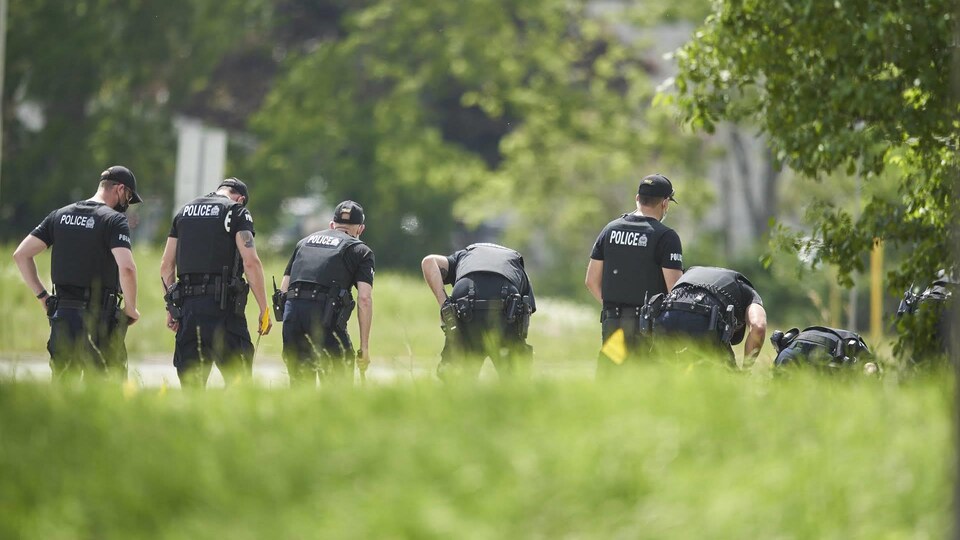 Une file de policiers recherche des preuves sur les lieux d'un accident de voiture à London, en Ontario, le lundi 7 juin 2021.