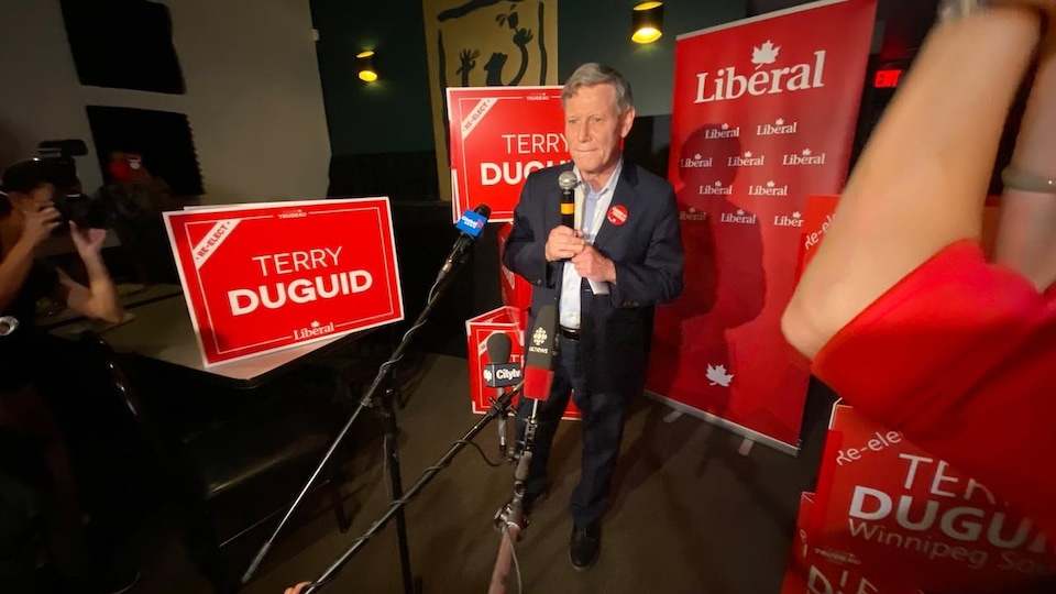 M. Duguid debout devant plusieurs pancartes portant son nom.