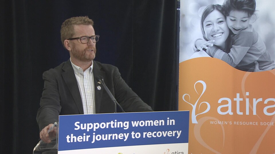Terry Lake derrière un podium où l'on peut lire en anglais " soutenir les femmes dans la voie de leur rétablissement".