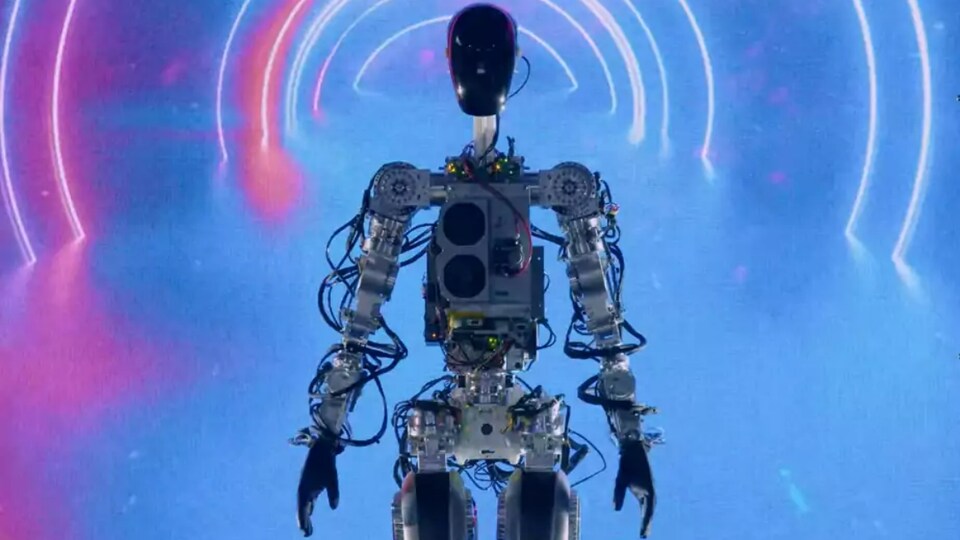 Un robot humanoïde marche dans un écran de fumée devant des néons rouge et bleu. 