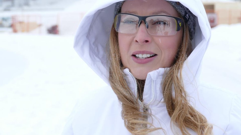 Une femme blonde porte des lunettes et un manteau blanc.  