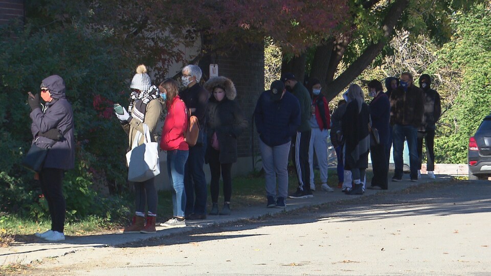 Des personnes portant le masque sont en ligne sur un trottoir.