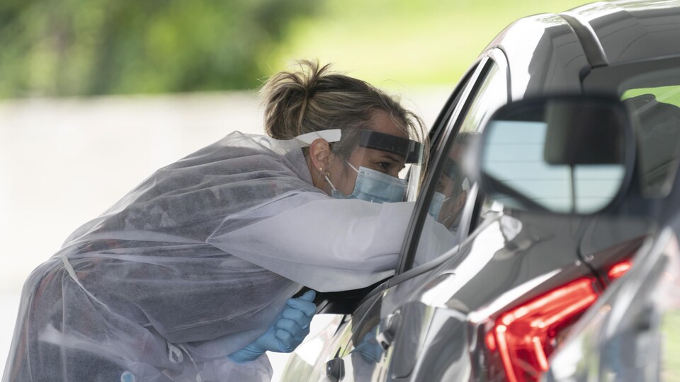 Une infirmière tend un écouvillon à l'intérieur d'une voiture.