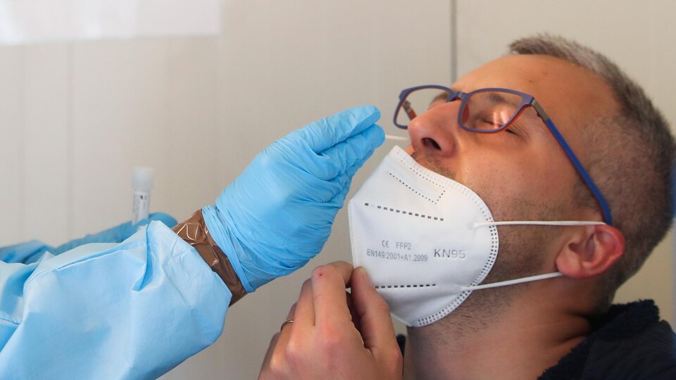 Un homme abaisse son masque et incline sa tête vers l'arrière pour qu'un échantillon soit prélevé dans sa narine.