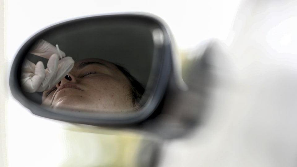Le visage d'une personne la tête inclinée vers l'arrière pendant un test de dépistage de COVID apparaît dans le rétroviseur d'une voiture.