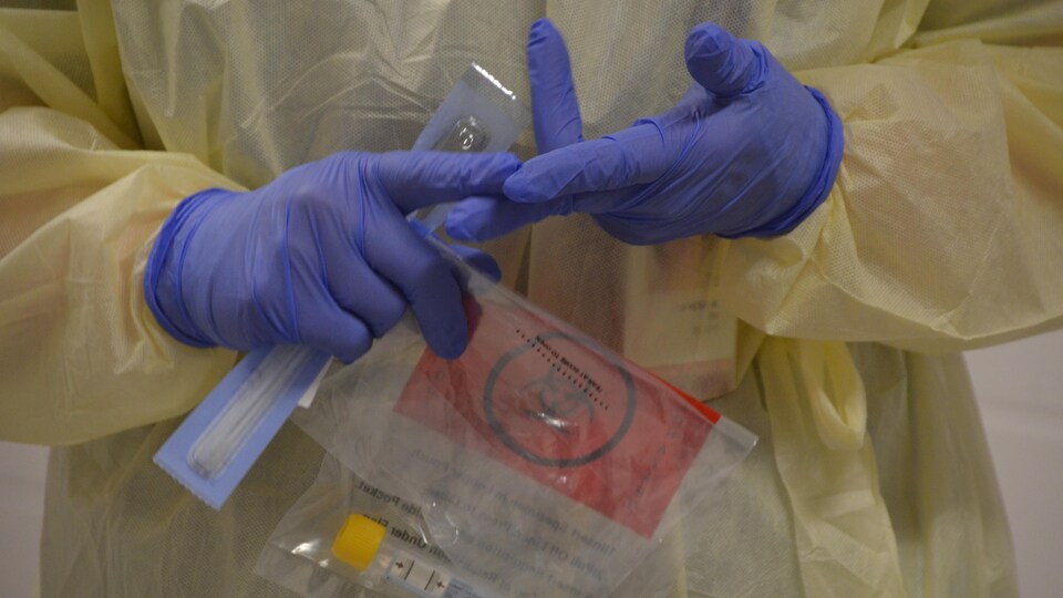 Une femme en équipement de protection tient dans ses mains une trousse de dépistage.