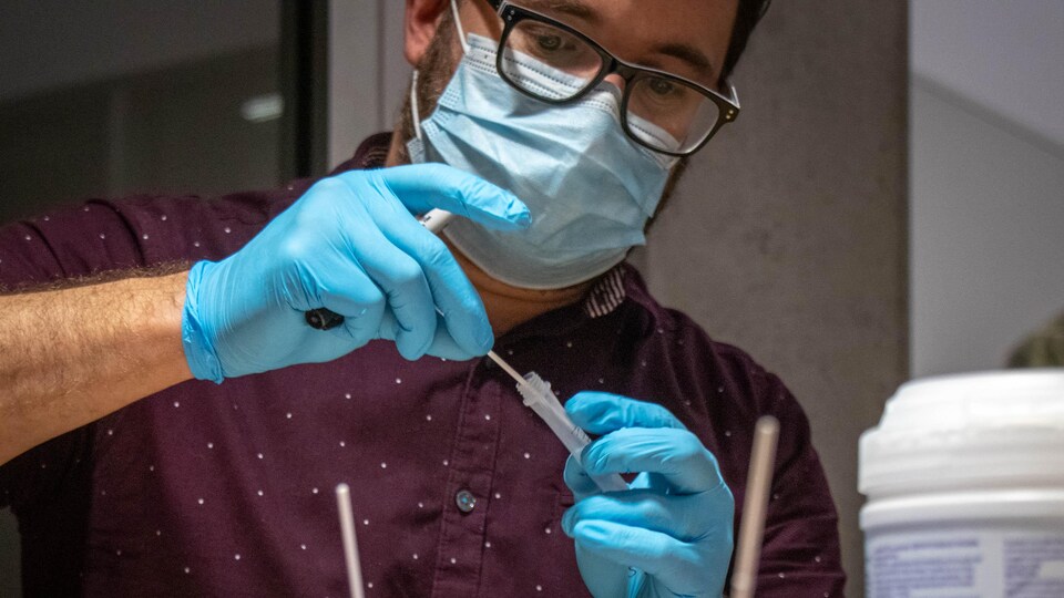 Un technicien de laboratoire portant un masque médical et des gants manipule un échantillon pour un test de dépistage.