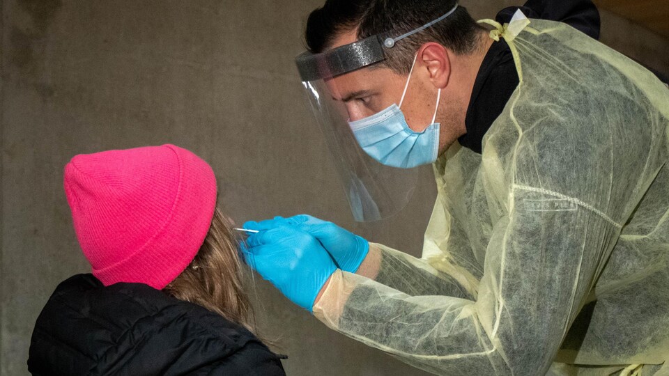 Un travailleur de la santé prélève un échantillon sur une femme, de dos.