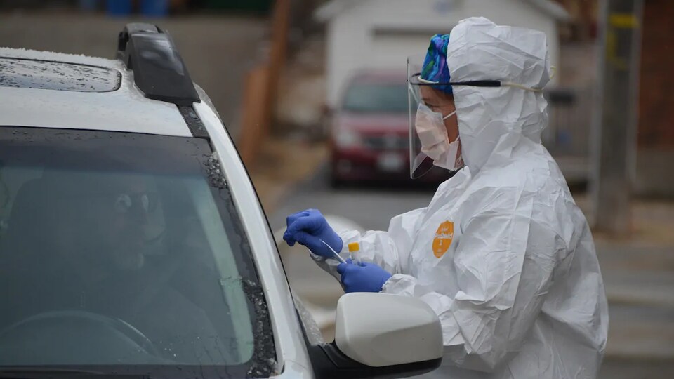 Une personne portant des équipements de protection effectue un test de dépistage de la COVID-19 pour un homme dans une voiture.