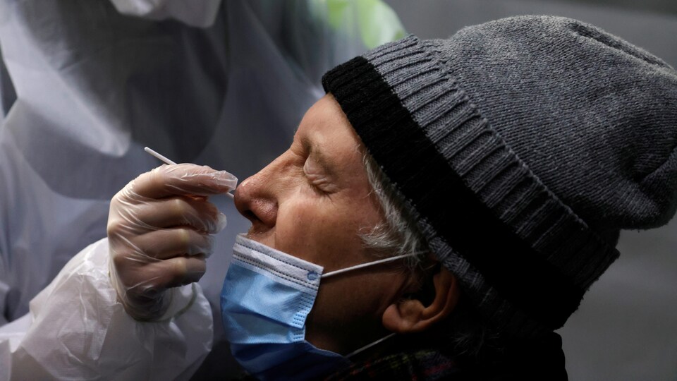 Une infirmière prélève un échantillon de la narine d'un homme qui porte une tuque.