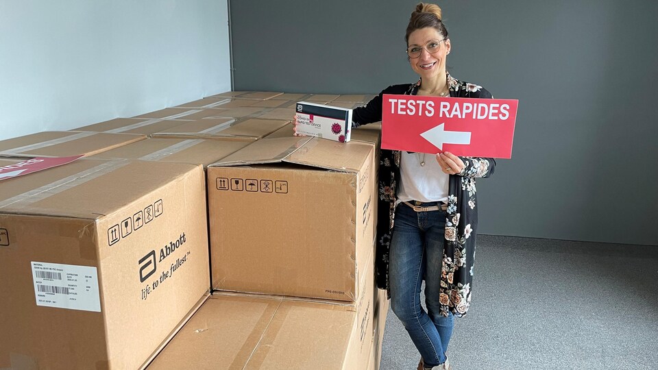 Une femme pose à côté de boîtes de test rapides.