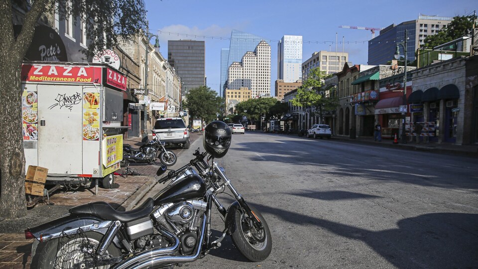 Une rue bordée de commerces et de bars et deux motos stationnées.