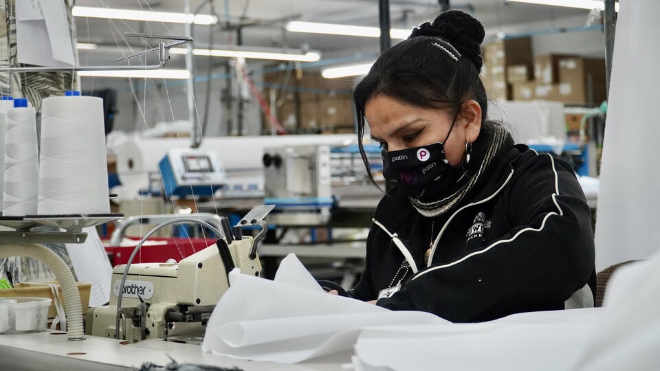 Une couturière avec un masque qui coud une blouse de protection dans l'usine.