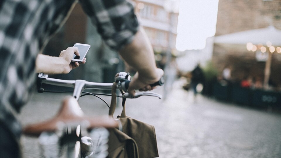 Un cycliste utilise son téléphone portable alors qu'il se trouve à côté de sa bicyclette. Il se trouve sur une place publique.