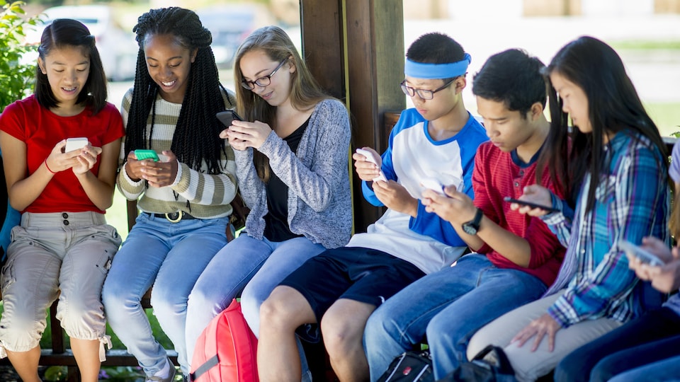Un groupe de jeunes multiethniques assis sur un banc en train d'utiliser leur téléphone intelligent.