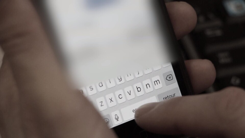 Une main tient un téléphone intelligent et un doigt appuie sur l'écran pour rédiger un message texte ou texto.