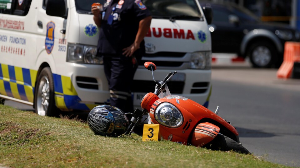 Une motocyclette tombée au sol devant un véhicule d'urgence.