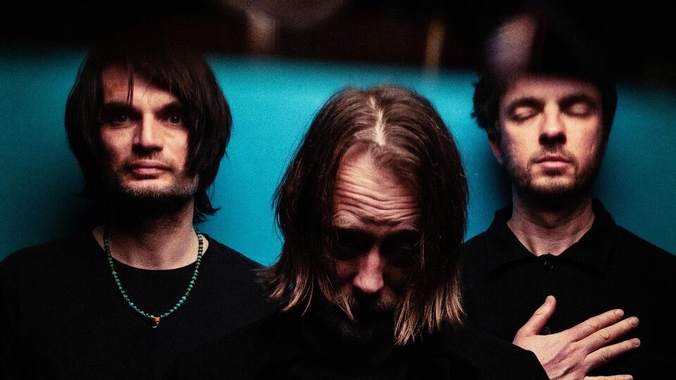 Les trois hommes posent sur un fond bleu.