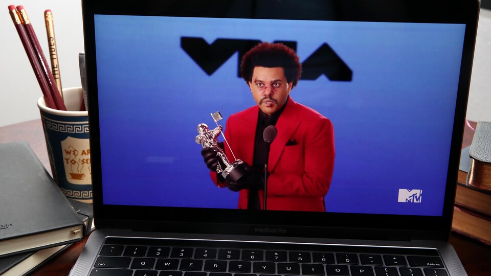 Un homme vêtu d'un veston rouge tient une statuette des MTV Video Music Awards sur scène. Dans la photo, la cérémonie est vue à partir de l'écran d'un ordinateur portable.