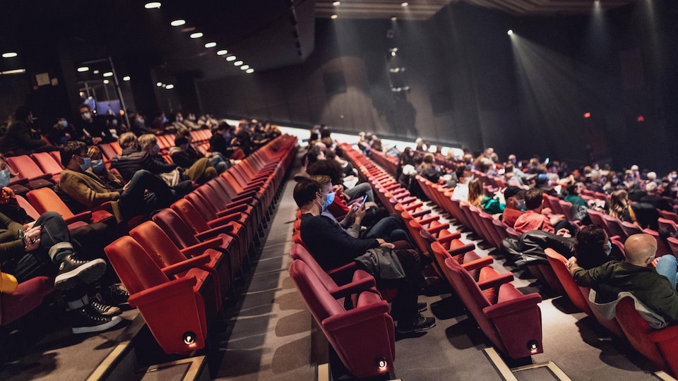Des personnes masquées sont assises dans une salle de spectacle.