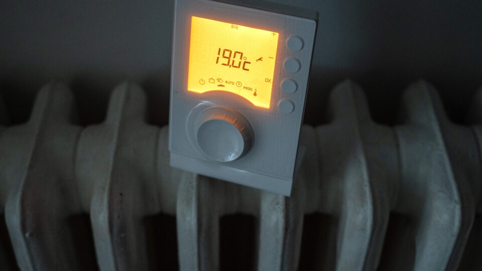 Un thermostat réglé à 19 degrés Celsius posé sur un radiateur en fer, peint en blanc, dans un appartement.