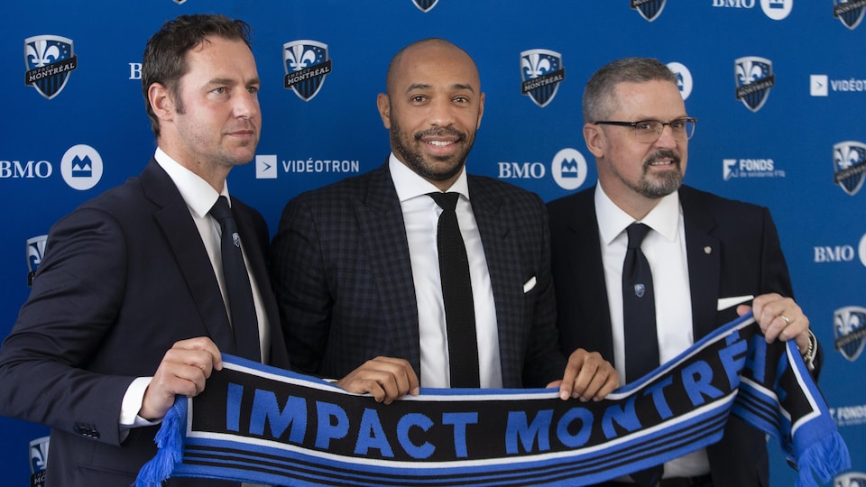 Trois hommes tiennent une écharpe sur laquelle est écrit Impact de Montréal.