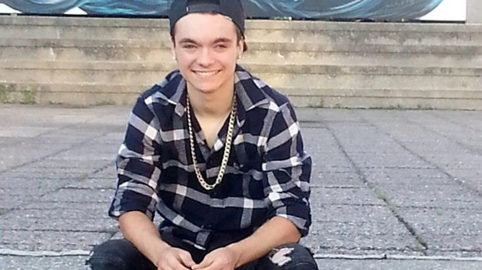 Le jeune homme assis à l'extérieur, souriant.