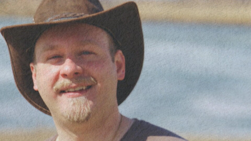 Un homme avec un chapeau de cowboy sourit.