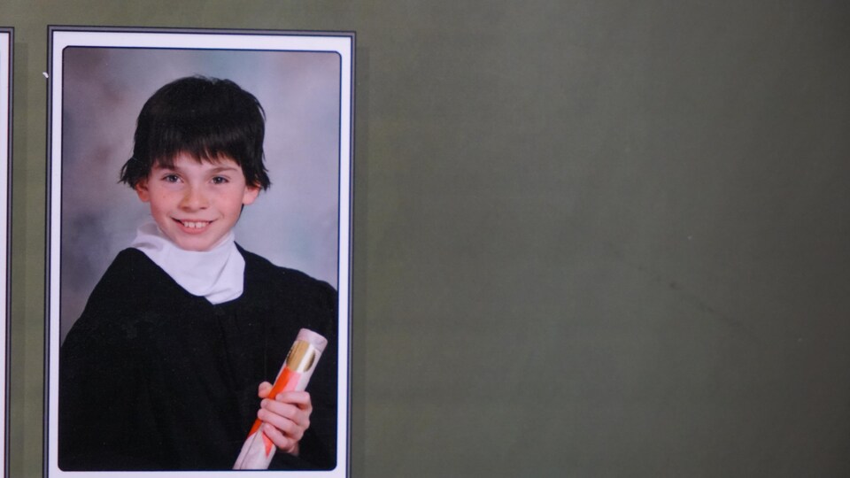 Un garçon souriant tient un diplôme, enveloppé dans une grande toge noire à col blanc.