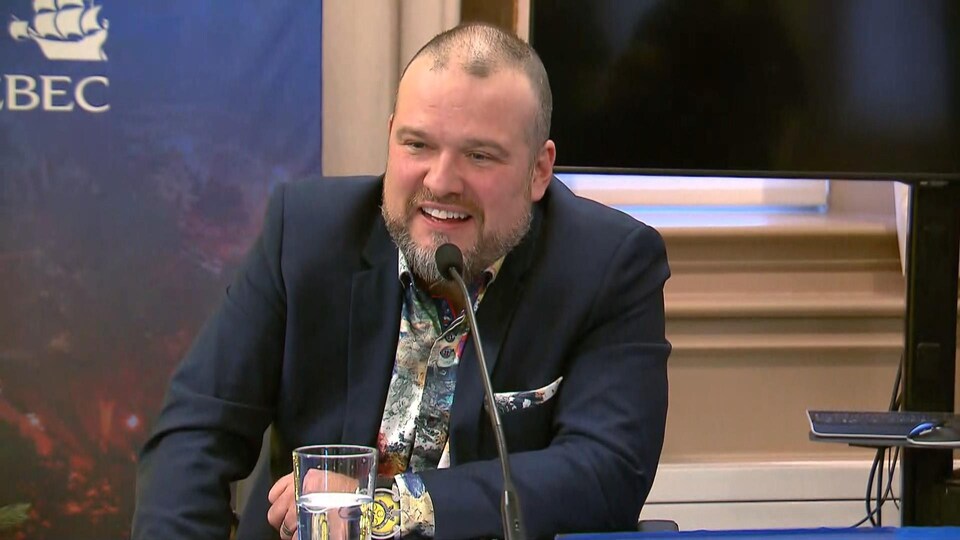 Plan rapproché de Thomas Wilson en veste et chemise fleurie, souriant.