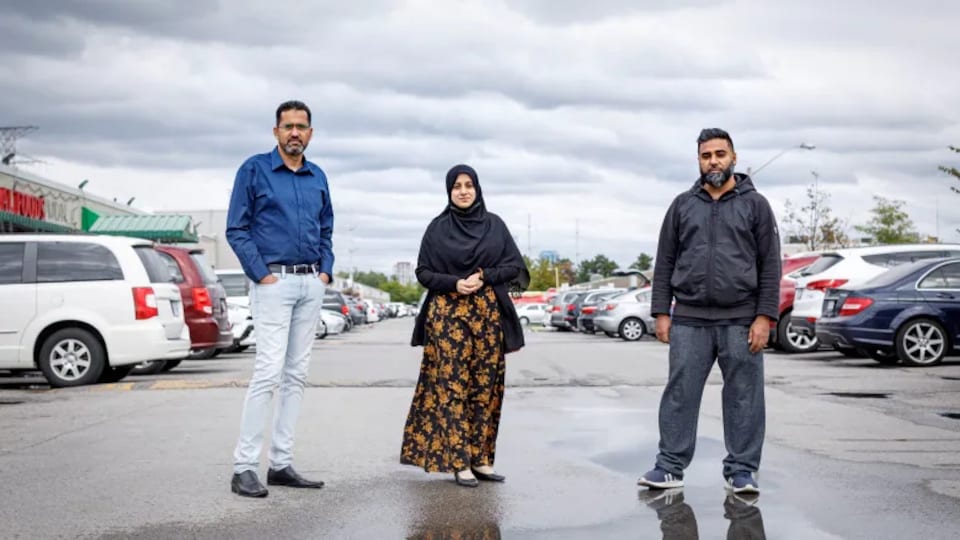Trois personnes se tiennent debout dans un stationnement.