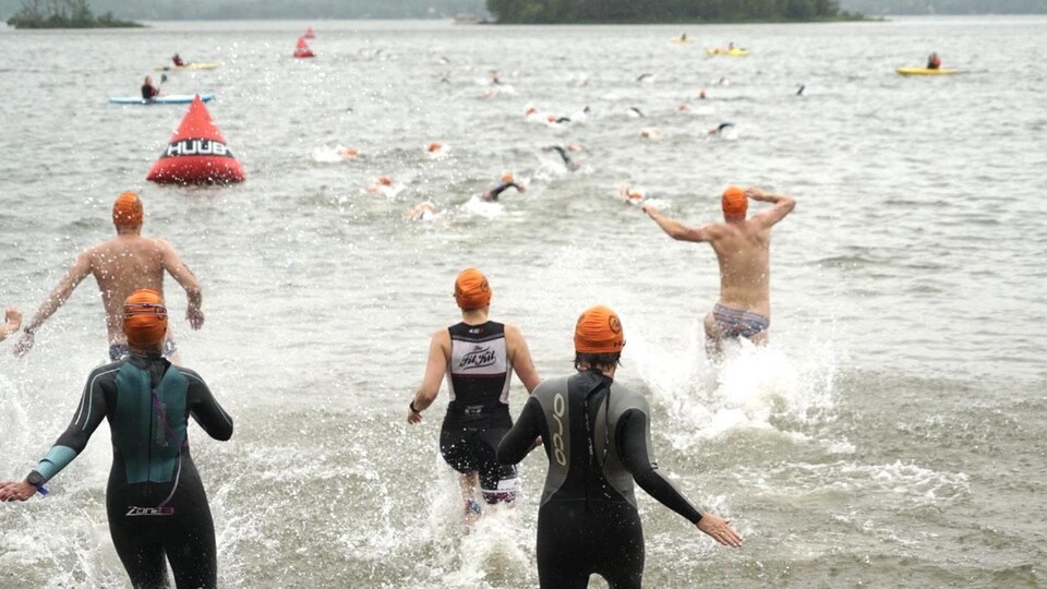 Des participants commencent l'étape de la natation en courant dans l'eau.