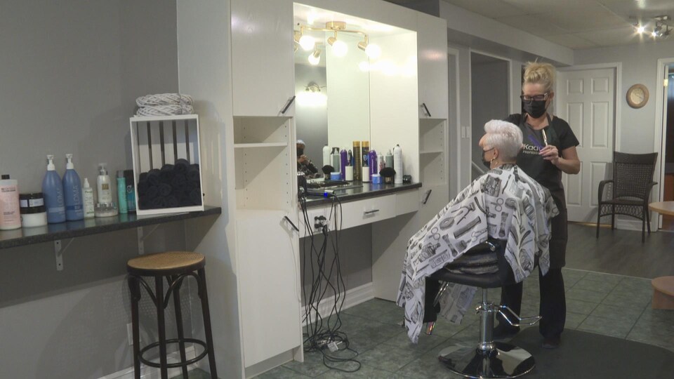 Une femme coupe les cheveux d'une autre femme assise dans un fauteuil.