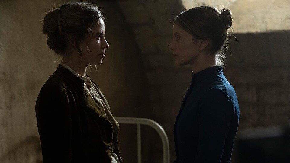 2 femmes portant des vêtements du 19e siècle se tiennent debout l'une en face de l'autre.