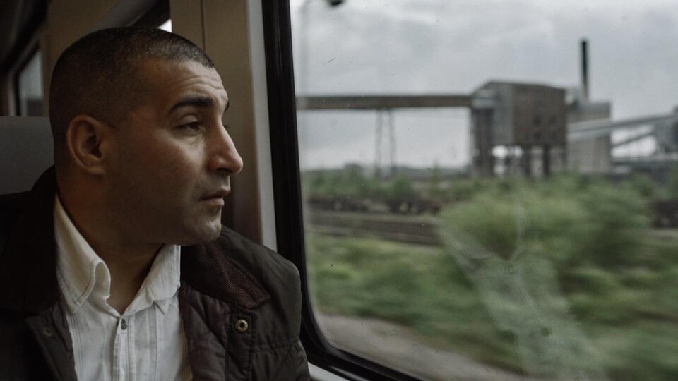Un homme assis dans un train regarde au dehors par la fenêtre.