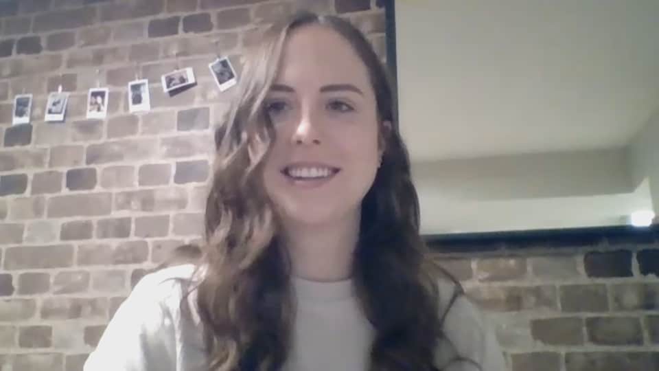 Une jeune femme en vidéoconférence devant un mur de briques.