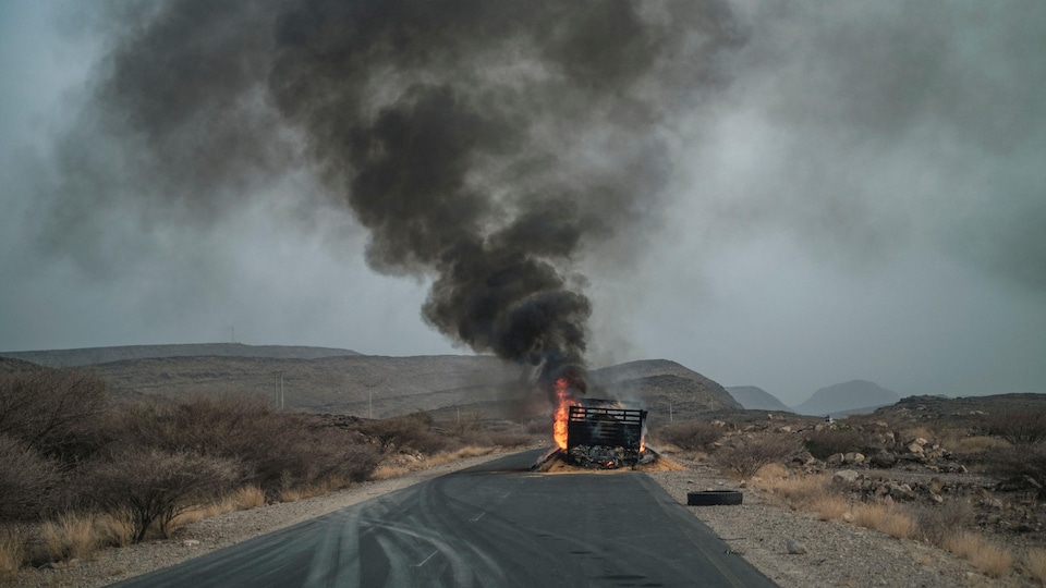 Un camion en feu sur une route dans un paysage désertique génère un nuage de fumée.