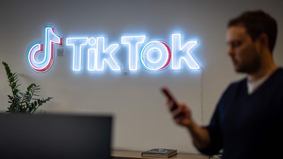 Un homme regarde son téléphone devant une enseigne lumineuse TikTok.