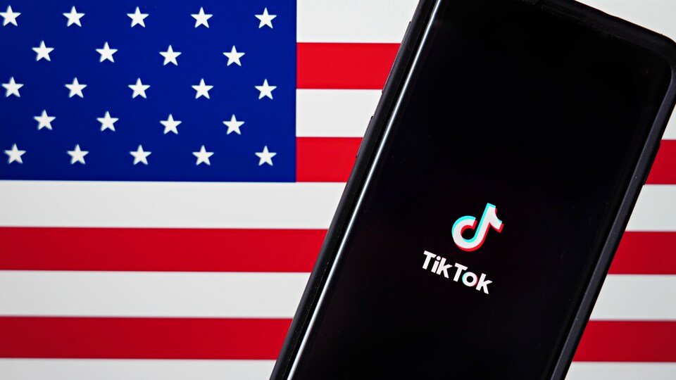 Un téléphone affichant le logo de TikTok, devant le drapeau des États-Unis.