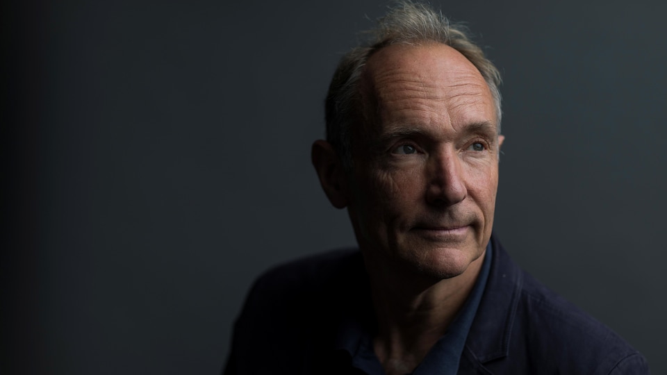 Une photo de Tim Berners-Lee, un homme aux cheveux gris avec une légère calvitie portant un veston bleu marine. Il regarde vers la droite d'un air pensif.