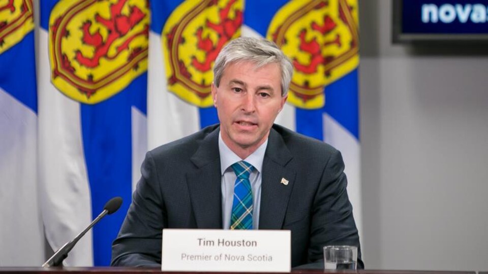Tim Houston est assis devant des drapeaux de la Nouvelle-Écosse.