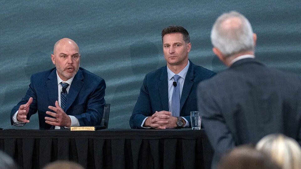 Tim Mills speaks as the two listen.