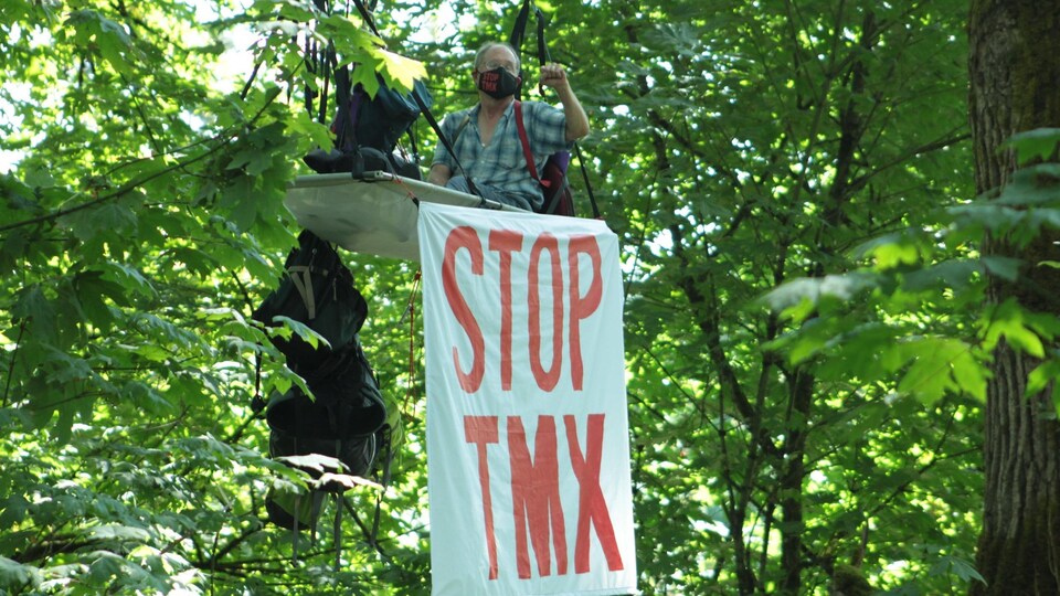 Le Dr Tim Takaro sur une plateforme dans un arbre avec une bannière où l'on peut lire Stop TMX.