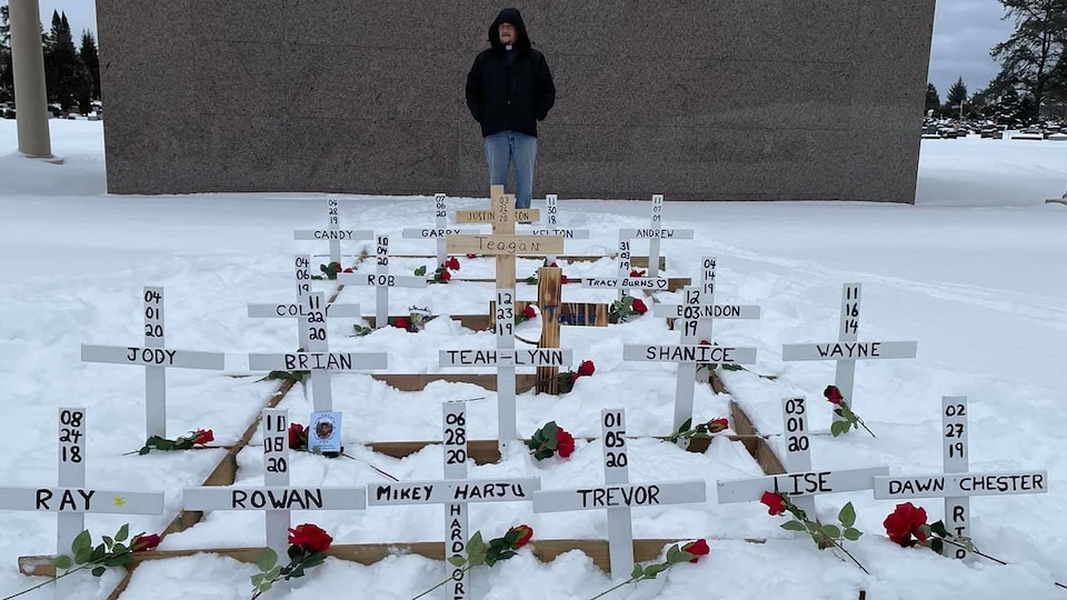 Des croix blanches sont plantées dans la neige avec des roses et le nom des défunts.