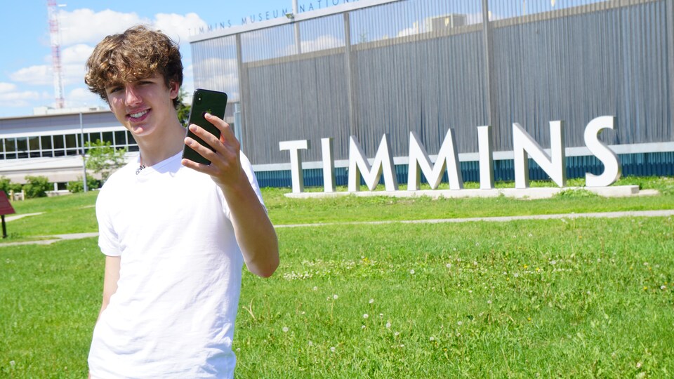Un jeune homme se prend en selfie devant le signe de Timmins.
