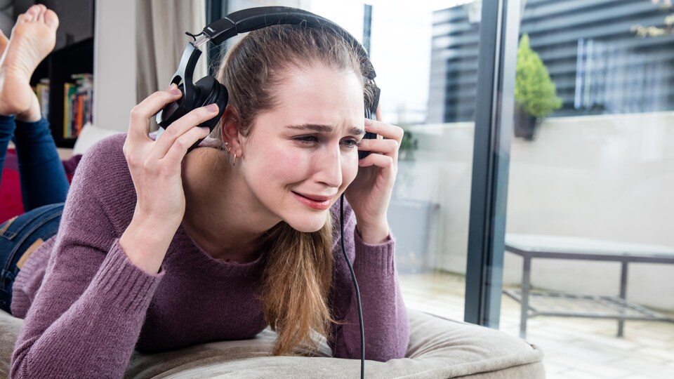 Une femme allongée sur le ventre pleure en enlevant ses écouteurs. 