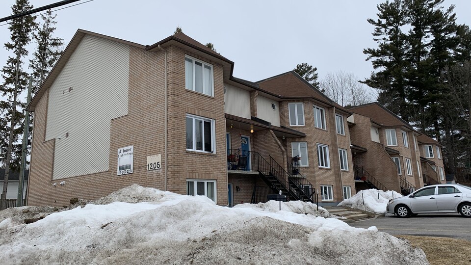 Un bâtiment résidentiel de trois étages avec un véhicule stationné devant. 